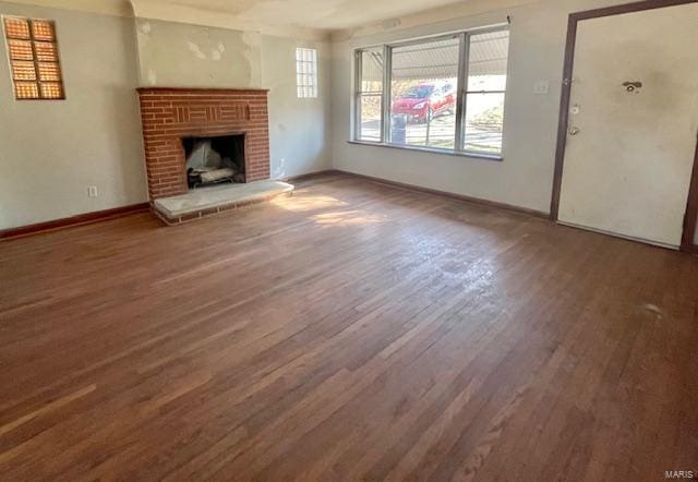 unfurnished living room with a brick fireplace, baseboards, and wood finished floors