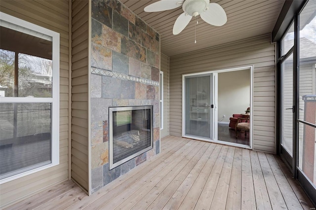 unfurnished sunroom featuring a tiled fireplace and ceiling fan