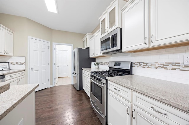 kitchen with white cabinets, dark wood finished floors, appliances with stainless steel finishes, glass insert cabinets, and light stone counters