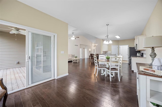 dining room with ceiling fan with notable chandelier, vaulted ceiling, and dark wood-style floors