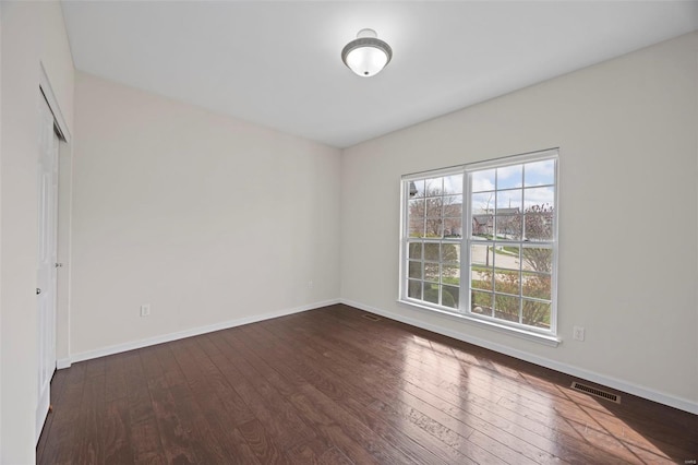 spare room with dark wood-type flooring, baseboards, and visible vents