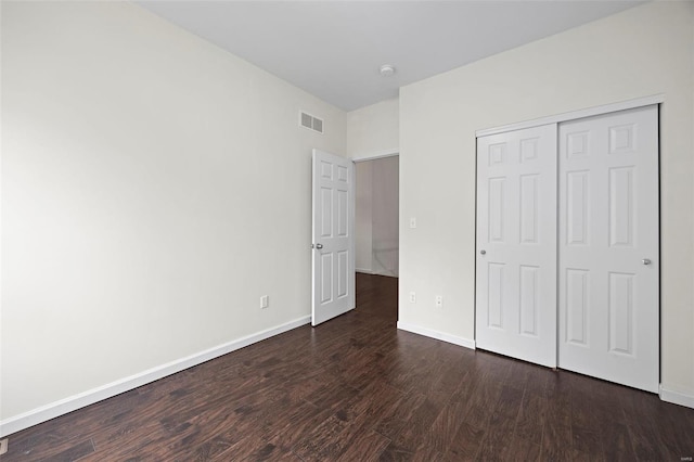 unfurnished bedroom with baseboards, dark wood-style flooring, visible vents, and a closet