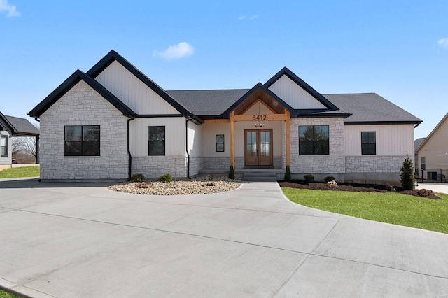 modern farmhouse featuring board and batten siding, a front yard, french doors, and stone siding