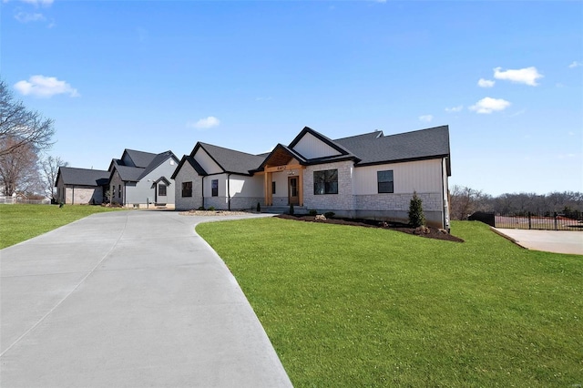 modern farmhouse style home featuring stone siding, concrete driveway, a front lawn, and fence