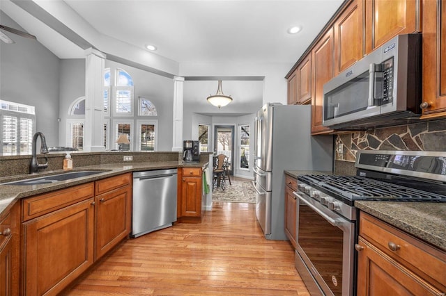 kitchen with brown cabinets, a sink, tasteful backsplash, light wood-style floors, and appliances with stainless steel finishes