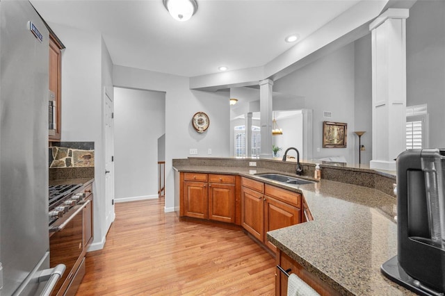 kitchen featuring light wood-type flooring, brown cabinets, stainless steel appliances, ornate columns, and a sink