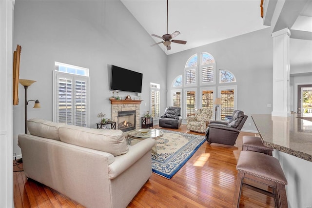 living room with a stone fireplace, light wood-style flooring, high vaulted ceiling, and a ceiling fan