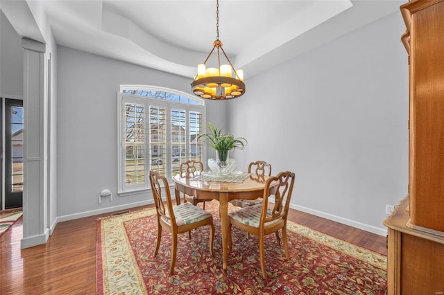 dining area featuring a tray ceiling, baseboards, a notable chandelier, and wood finished floors