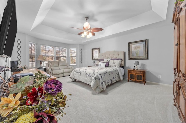 bedroom featuring baseboards, a raised ceiling, light colored carpet, and a ceiling fan