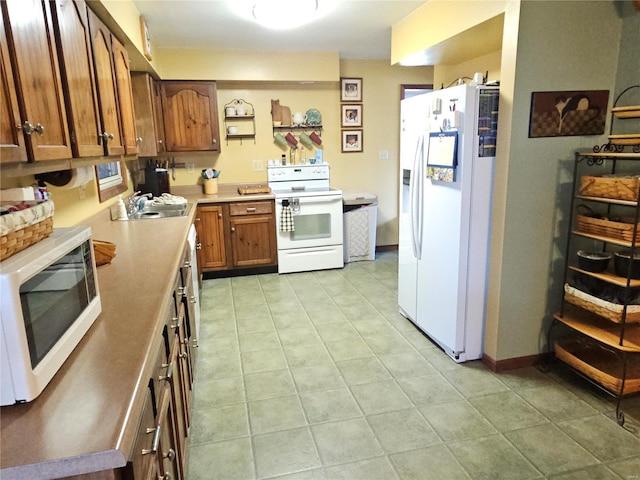 kitchen with a sink, white appliances, brown cabinetry, light countertops, and light tile patterned floors