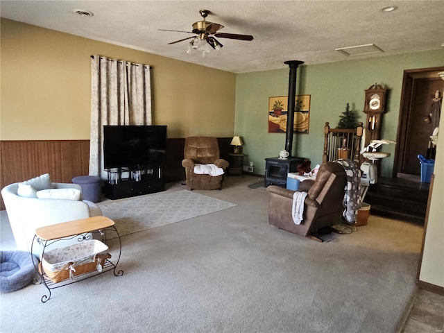 carpeted living room featuring visible vents, ceiling fan, attic access, wainscoting, and a wood stove