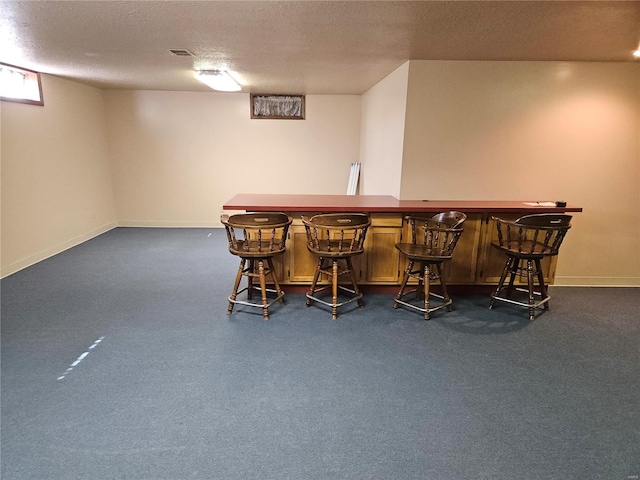 bar featuring visible vents, a textured ceiling, dark carpet, a bar, and baseboards