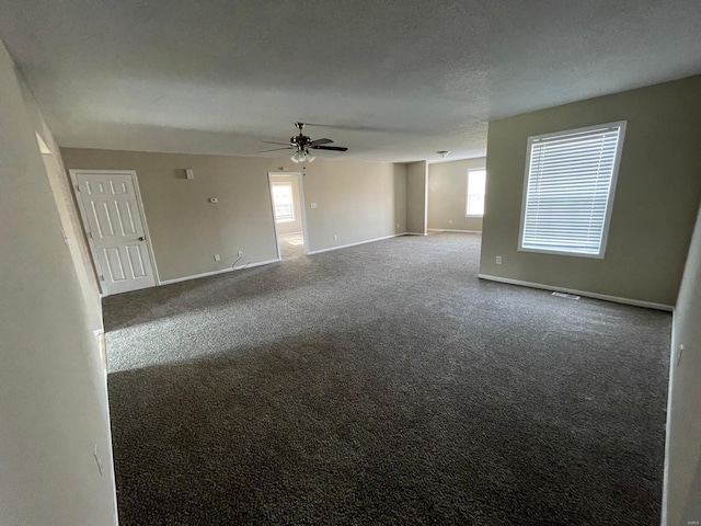 carpeted empty room with a healthy amount of sunlight, a textured ceiling, baseboards, and a ceiling fan