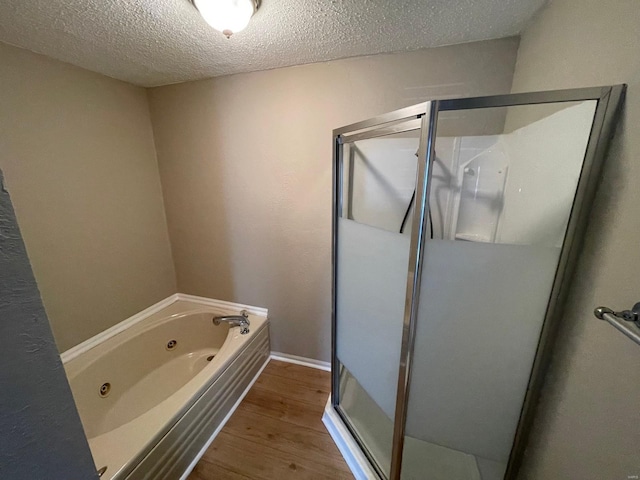 bathroom featuring wood finished floors, a textured ceiling, a jetted tub, and a stall shower