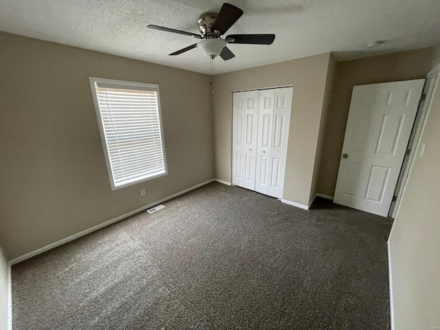 unfurnished bedroom with a textured ceiling, dark carpet, a closet, baseboards, and ceiling fan