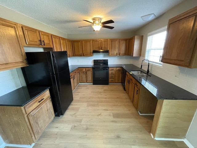 kitchen featuring dark countertops, brown cabinets, light wood-style floors, black appliances, and a sink