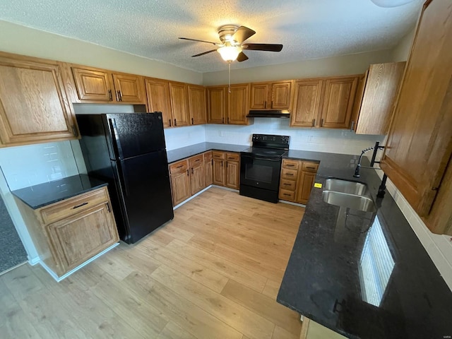 kitchen featuring a sink, black appliances, light wood-style floors, under cabinet range hood, and brown cabinets