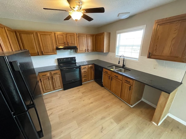 kitchen with light wood finished floors, under cabinet range hood, brown cabinets, black appliances, and a sink