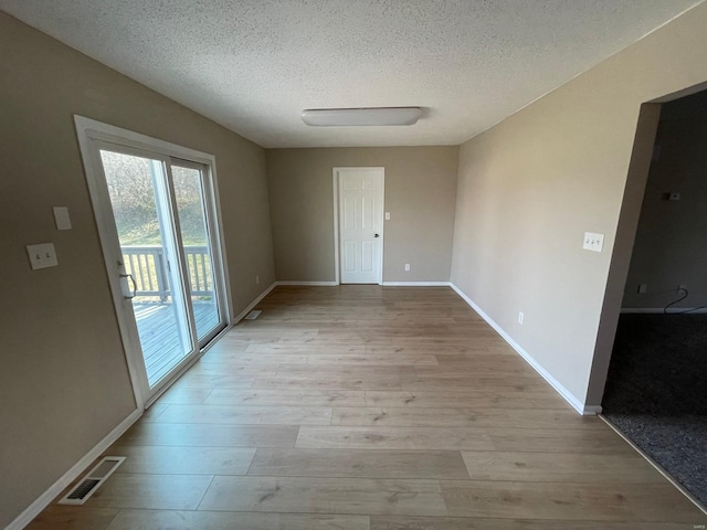 empty room featuring visible vents, a textured ceiling, baseboards, and wood finished floors