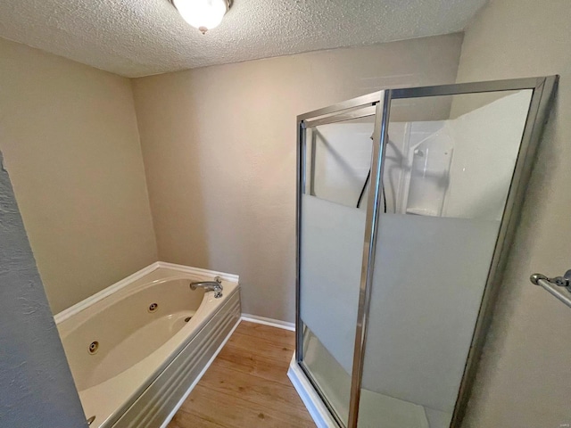 full bathroom featuring a textured ceiling, wood finished floors, a shower stall, baseboards, and a whirlpool tub