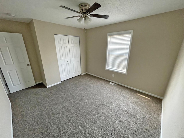 unfurnished bedroom with ceiling fan, baseboards, a closet, a textured ceiling, and dark colored carpet