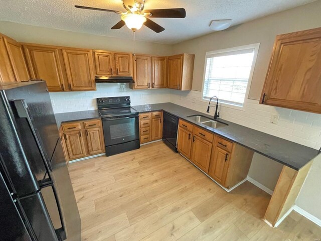 kitchen with black appliances, under cabinet range hood, a sink, dark countertops, and light wood finished floors