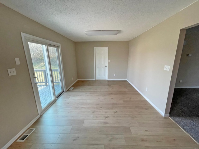 spare room featuring visible vents, a textured ceiling, light wood-type flooring, and baseboards