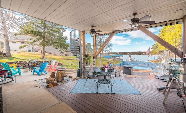 wooden deck featuring an outdoor fire pit, outdoor dining area, a water view, ceiling fan, and a yard
