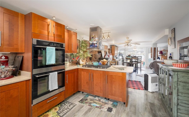 kitchen with light countertops, a peninsula, brown cabinets, stainless steel appliances, and island range hood