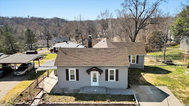 view of front facade with a shingled roof, a front lawn, a forest view, and a chimney