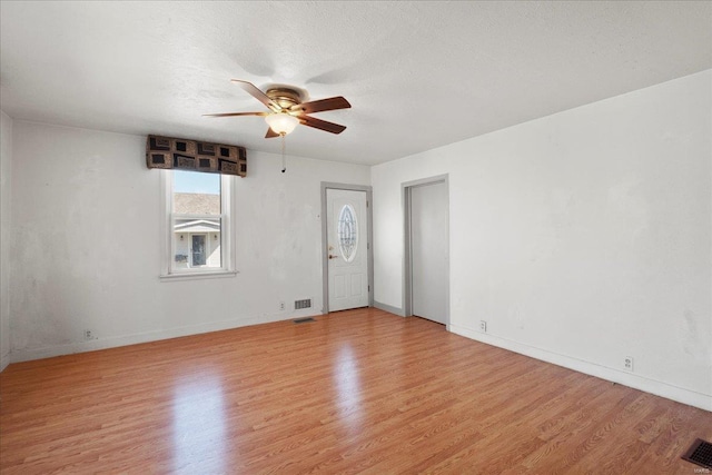 empty room featuring visible vents, baseboards, ceiling fan, light wood-type flooring, and a textured ceiling