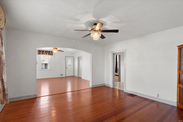 unfurnished living room featuring visible vents, hardwood / wood-style floors, arched walkways, baseboards, and ceiling fan