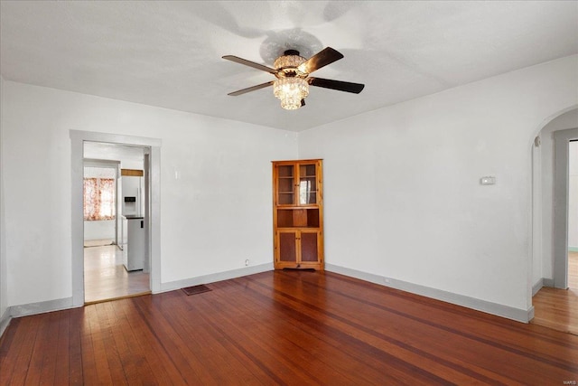 unfurnished room featuring baseboards, arched walkways, wood-type flooring, and ceiling fan