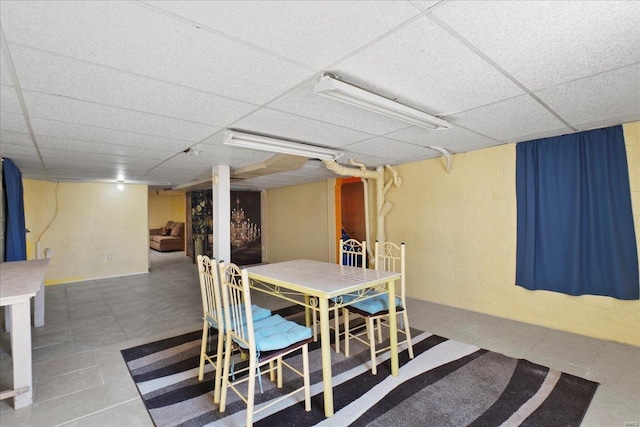 dining room with a drop ceiling, concrete block wall, and tile patterned flooring