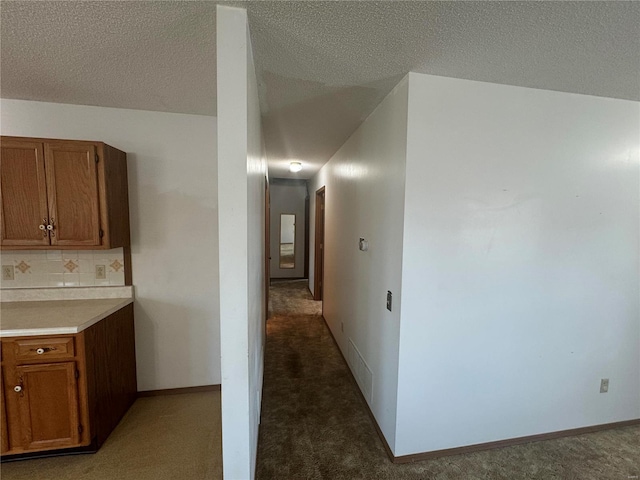 hall with light colored carpet, a textured ceiling, and baseboards