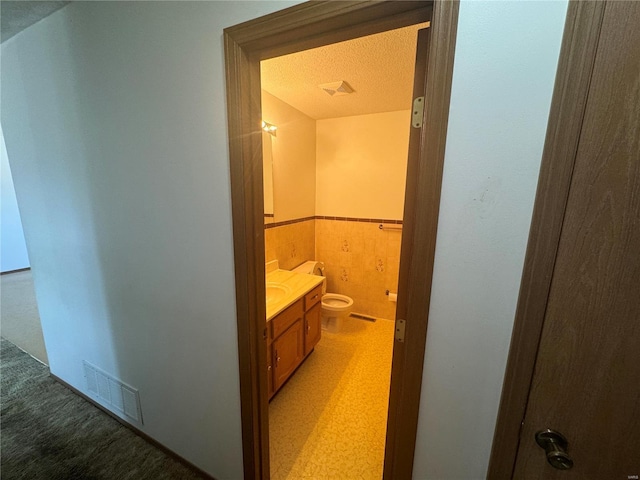 bathroom featuring visible vents, toilet, tile walls, wainscoting, and vanity