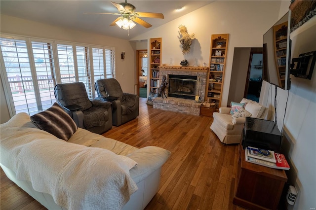 living room featuring ceiling fan, vaulted ceiling, a brick fireplace, and wood-type flooring