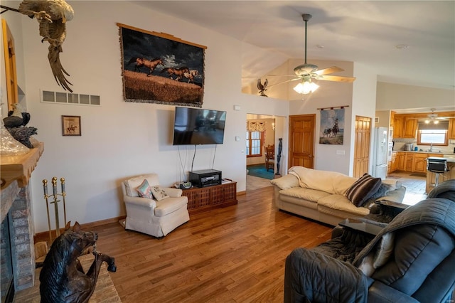 living room featuring light wood finished floors, visible vents, a ceiling fan, and high vaulted ceiling