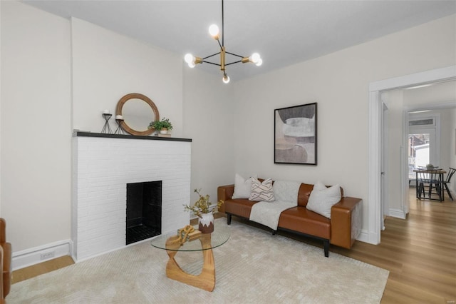 living room featuring a notable chandelier, a brick fireplace, baseboards, and wood finished floors