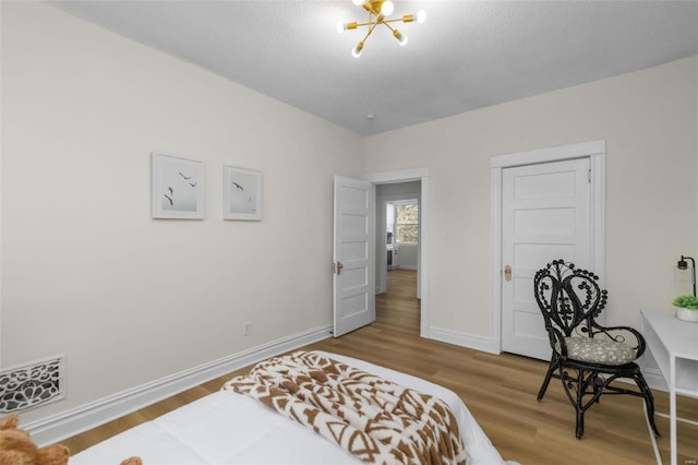 bedroom featuring visible vents, a textured ceiling, wood finished floors, an inviting chandelier, and baseboards