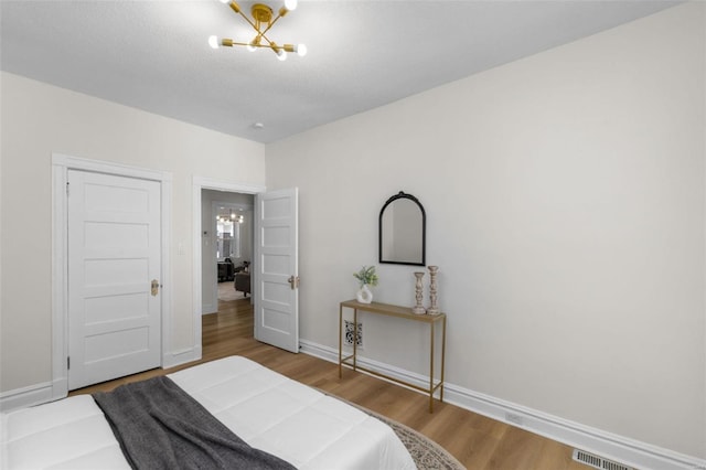 bedroom featuring baseboards, wood finished floors, visible vents, and a chandelier