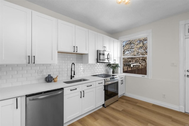 kitchen featuring a sink, stainless steel appliances, light countertops, white cabinetry, and light wood-type flooring