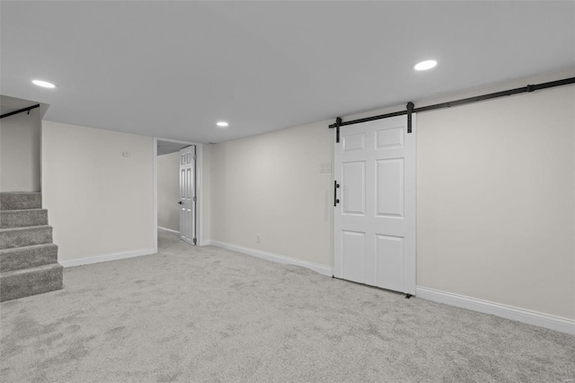 finished below grade area with a barn door, baseboards, carpet, and stairway