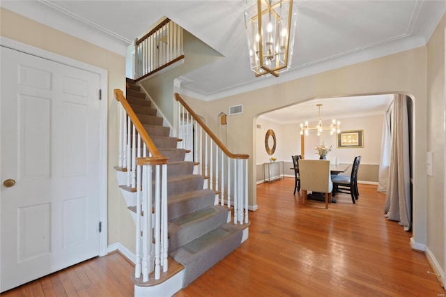 staircase featuring an inviting chandelier, crown molding, wood finished floors, and arched walkways