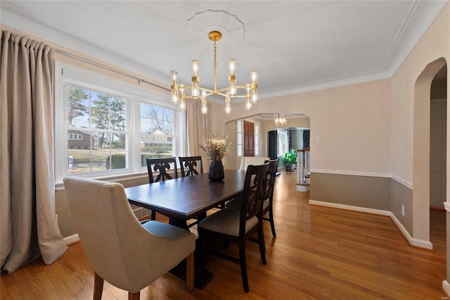 dining area with wood finished floors, baseboards, arched walkways, crown molding, and a notable chandelier