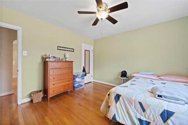 bedroom featuring ceiling fan, wood finished floors, arched walkways, and baseboards