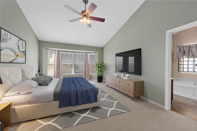 bedroom featuring light carpet, high vaulted ceiling, a ceiling fan, ensuite bath, and baseboards