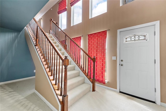 carpeted entryway with baseboards, stairs, and a towering ceiling