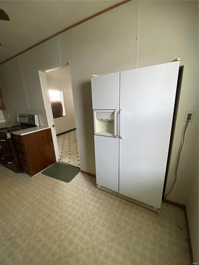 kitchen featuring light floors, white refrigerator with ice dispenser, electric range oven, and light countertops