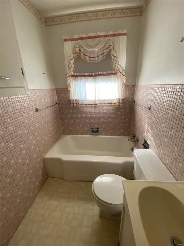 bathroom featuring toilet, tile walls, a bath, and wainscoting